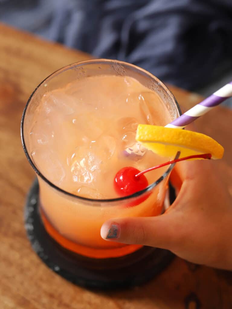 A small hand picking up a glass of mocktail.