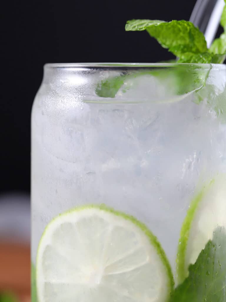 Close up of a glass filled with ice, soda, lime, and mint.