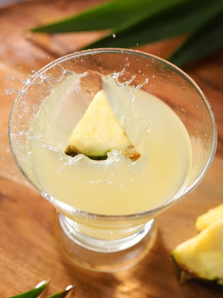 A piece of pineapple splashing into a cocktail glass.