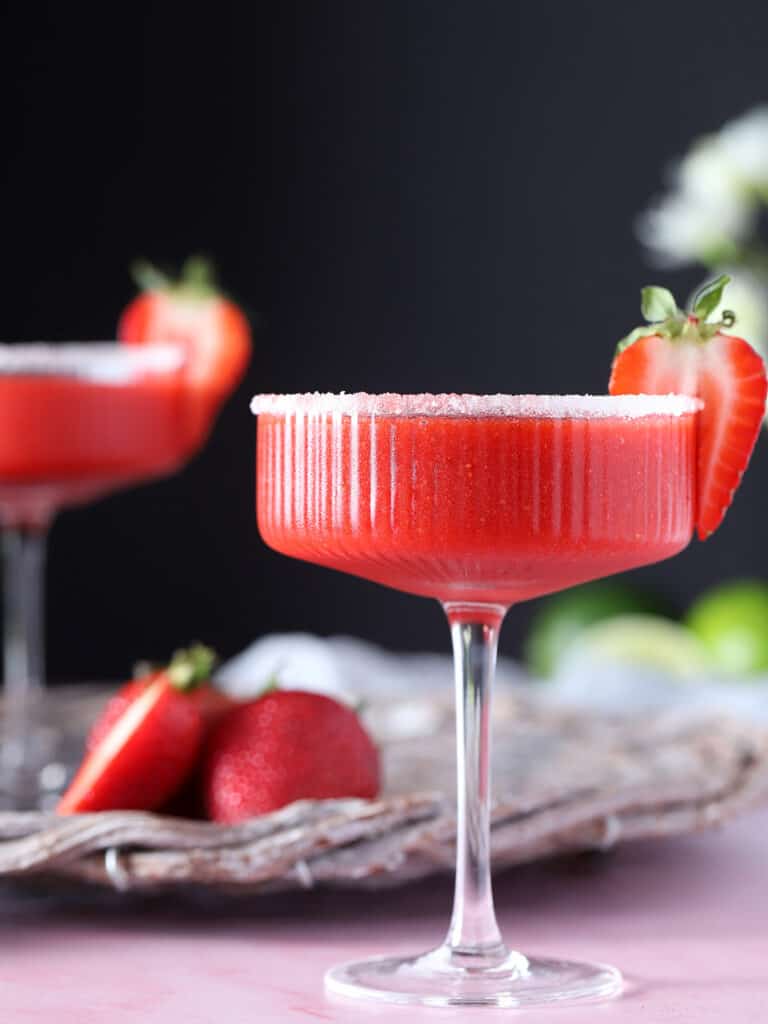 A glass filled with red cocktail, garnished with a strawberry.
