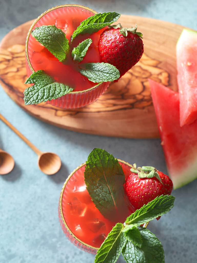 Mint leaves and strawberries in red drinks.