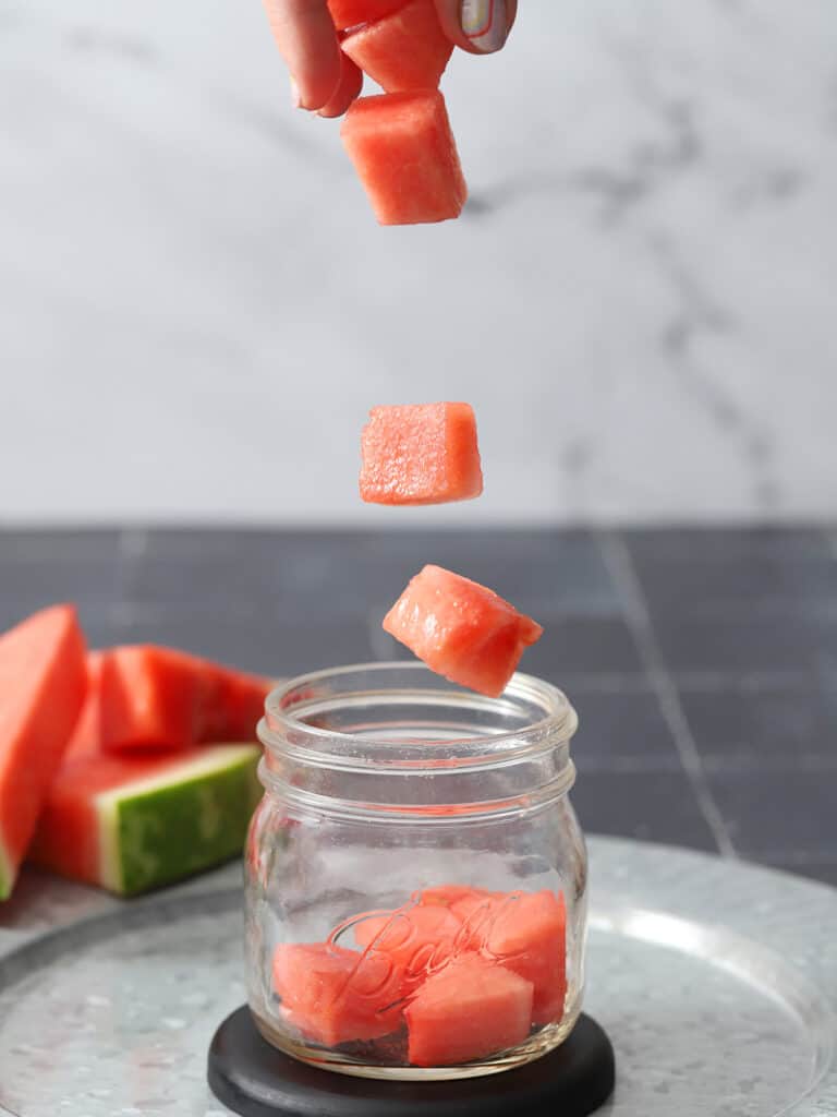 Watermelon chunks dropping into a mason jar.
