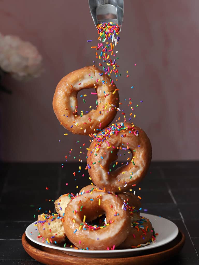 Sprinkled being poured over a stack of donuts.